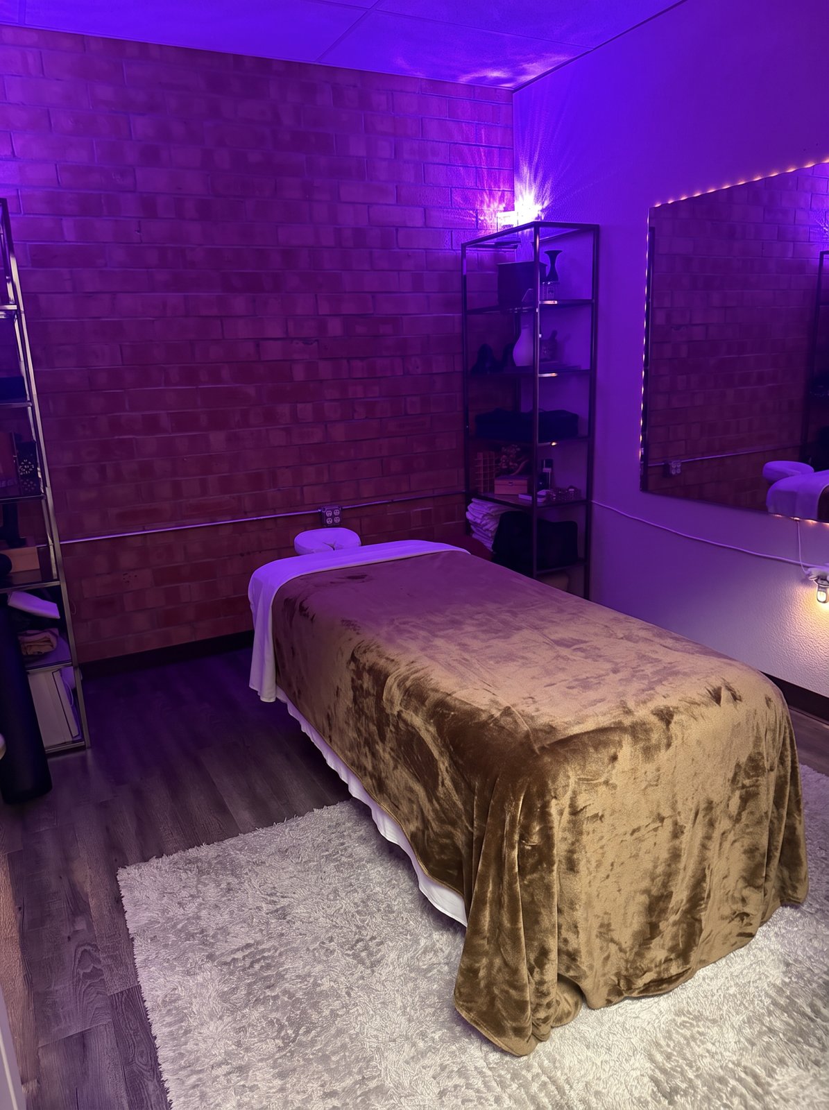 Jorgé’s treatment room with the massage table, brick wall, glass shelves, and purple ambient lighting