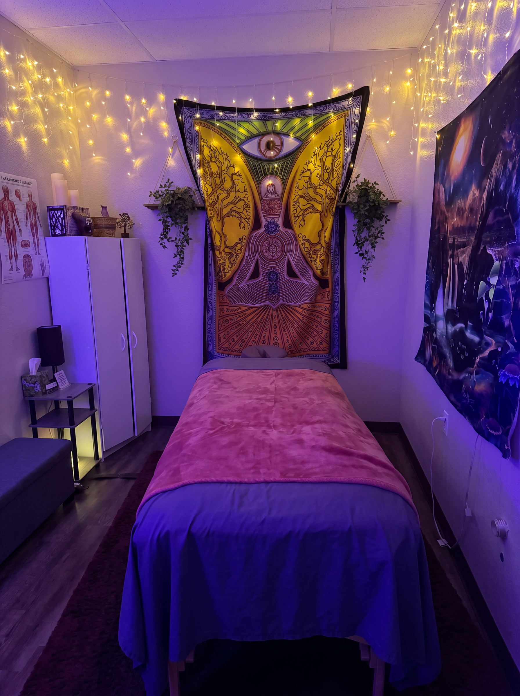 Landon's treatment room with his massage table, string lights, meditation tapestry, plants, and galaxy artwork