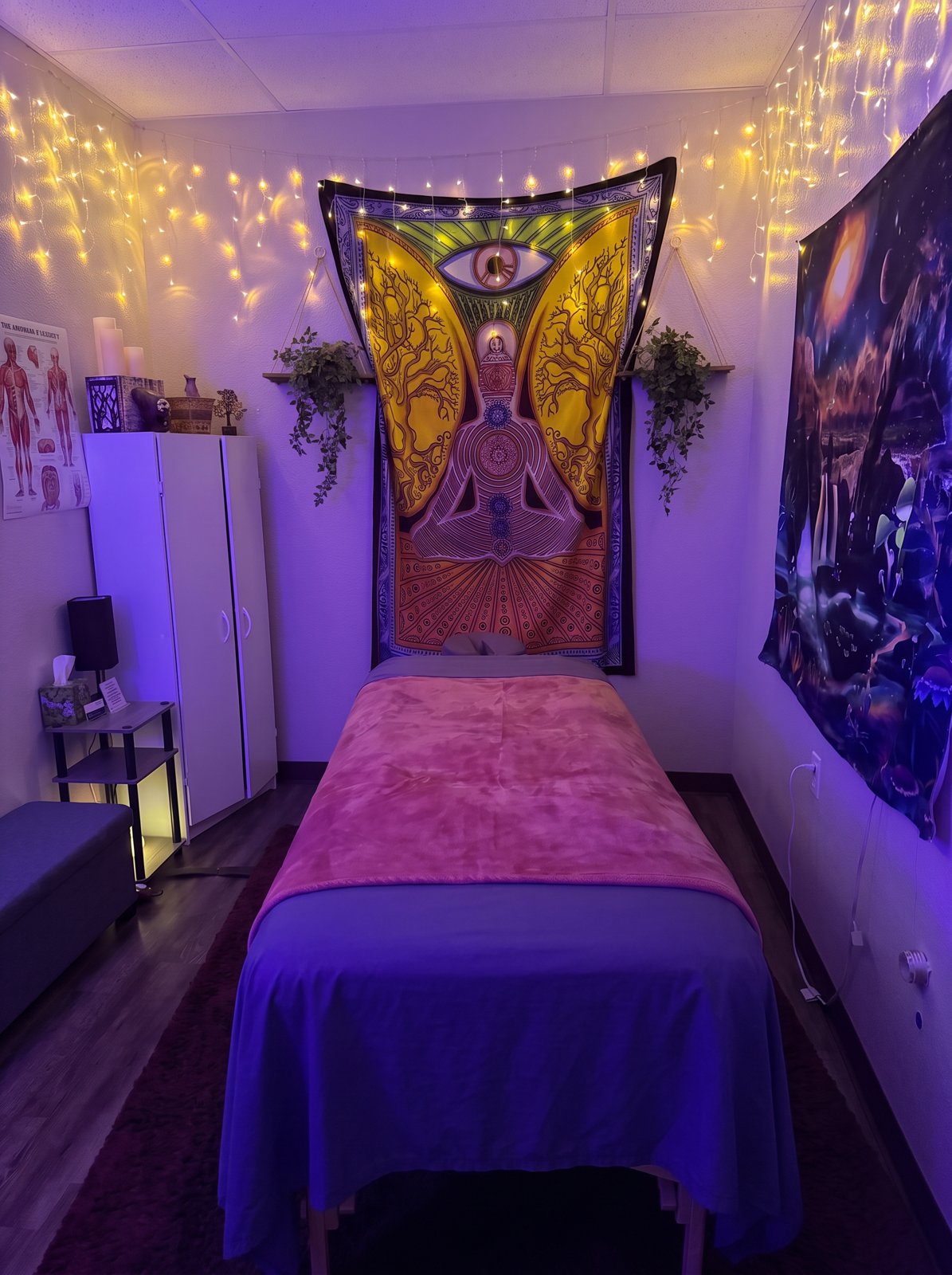 Landon's treatment room with his massage table, string lights, meditation tapestry, plants, and galaxy artwork