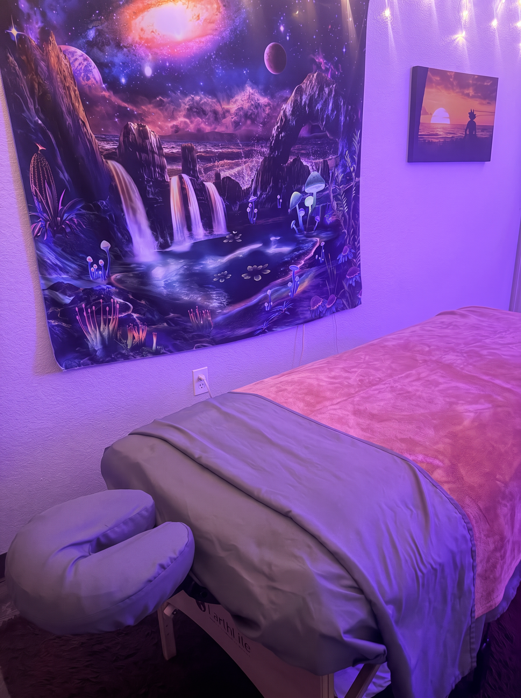 Landon's massage table with gray linens and a face cradle, beside the galaxy tapestry and framed picture