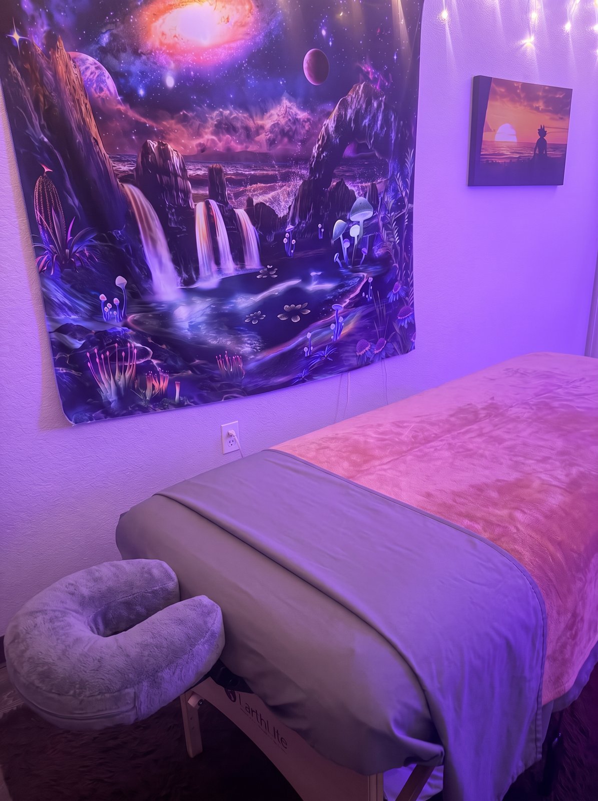 Landon's massage table with gray linens and a face cradle, beside the galaxy tapestry and framed picture